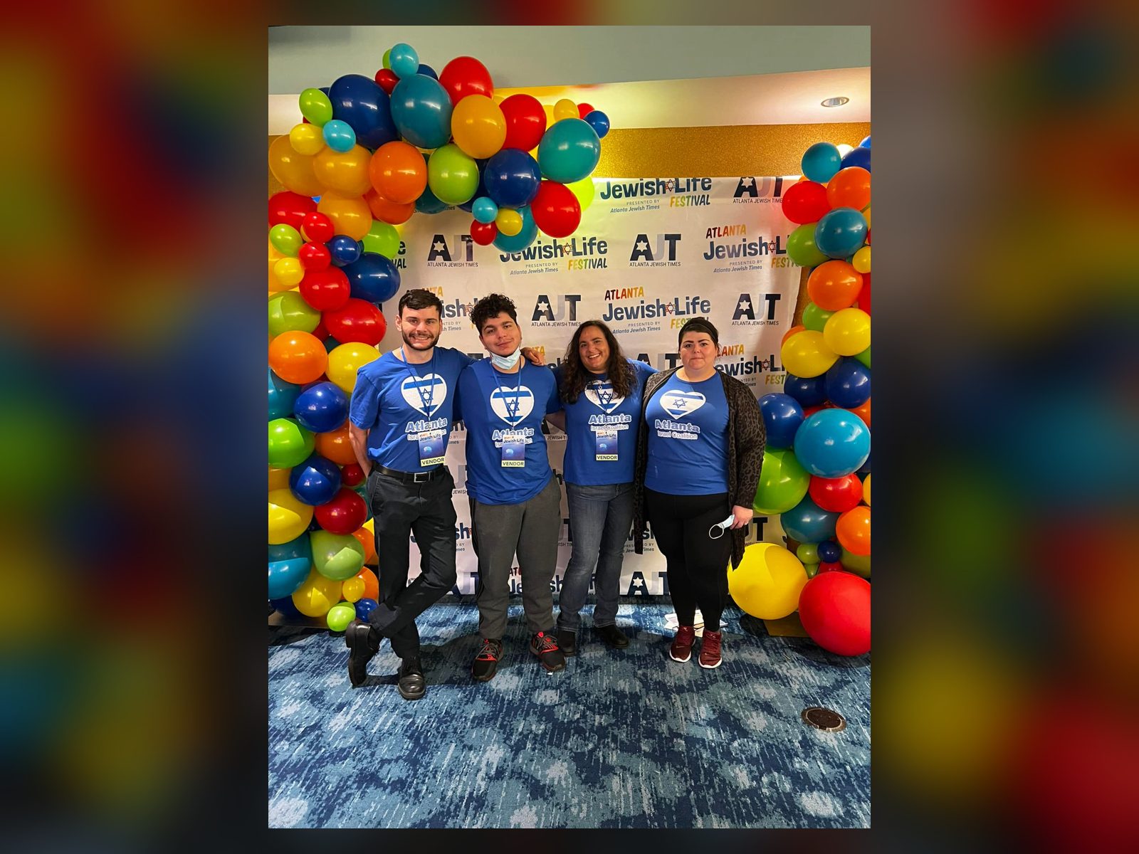 Four AIC volunteers in Atlanta Israel Coalition T-shirts in front of a balloon arch at the Atlanta Jewish Life Festival.