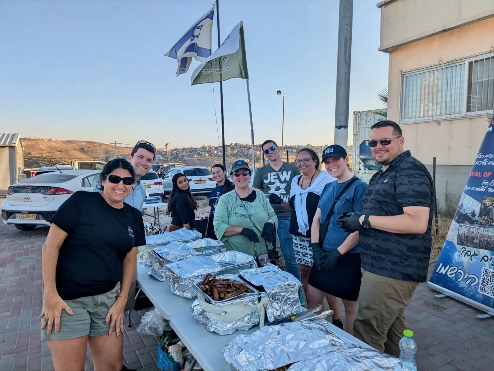 Atlanta Israel Coalition volunteers prepare and serve food outdoors in Israel, an Israeli flag flying behind them.